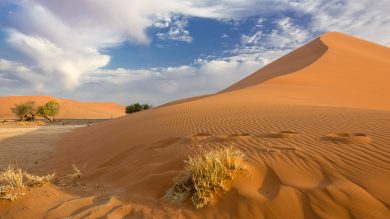 orange Sanddüne vor blauem Himmel mit Wolken