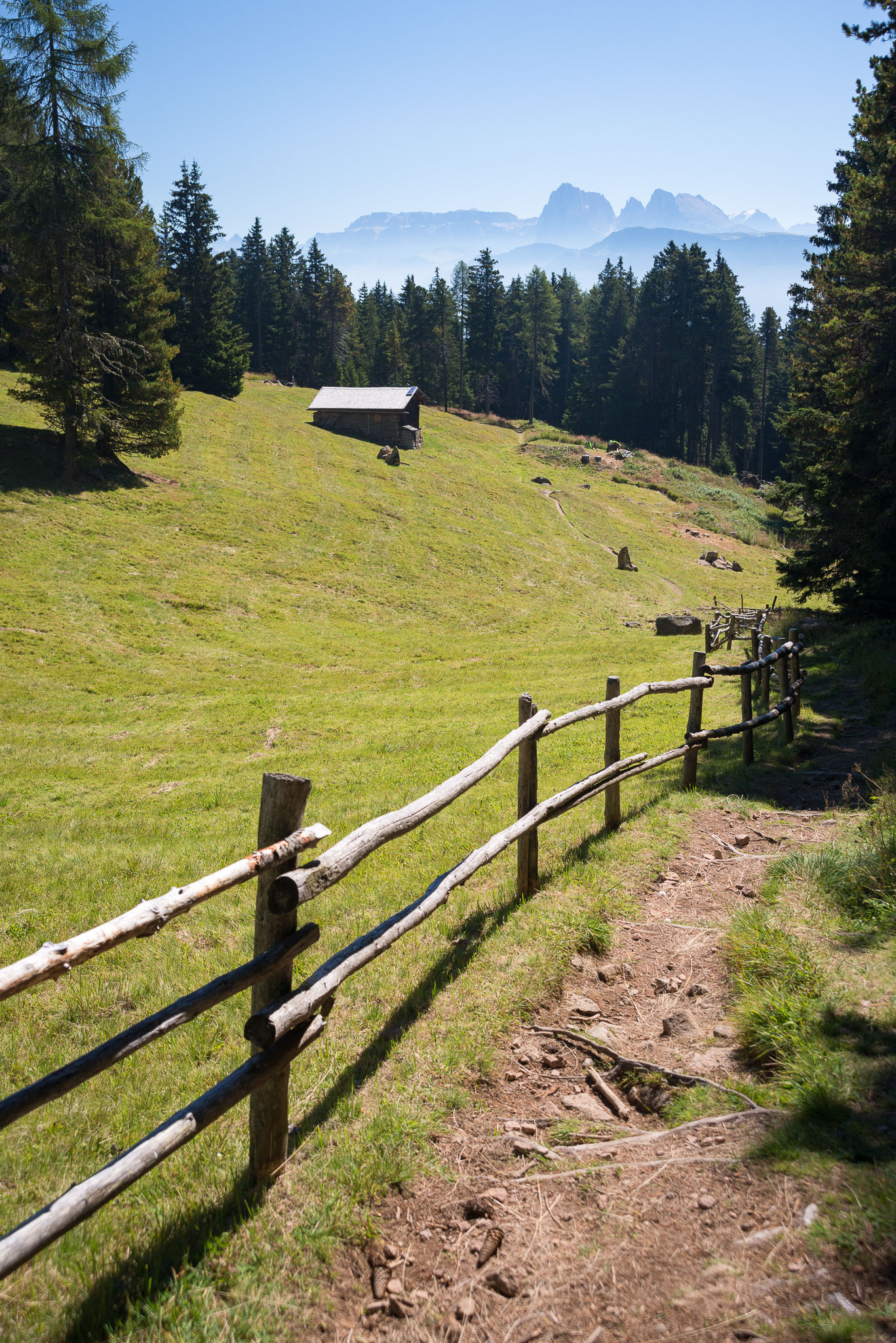 Wanderweg mit Blick auf eine Almhütte und die dahinterliegenden Dolomiten.